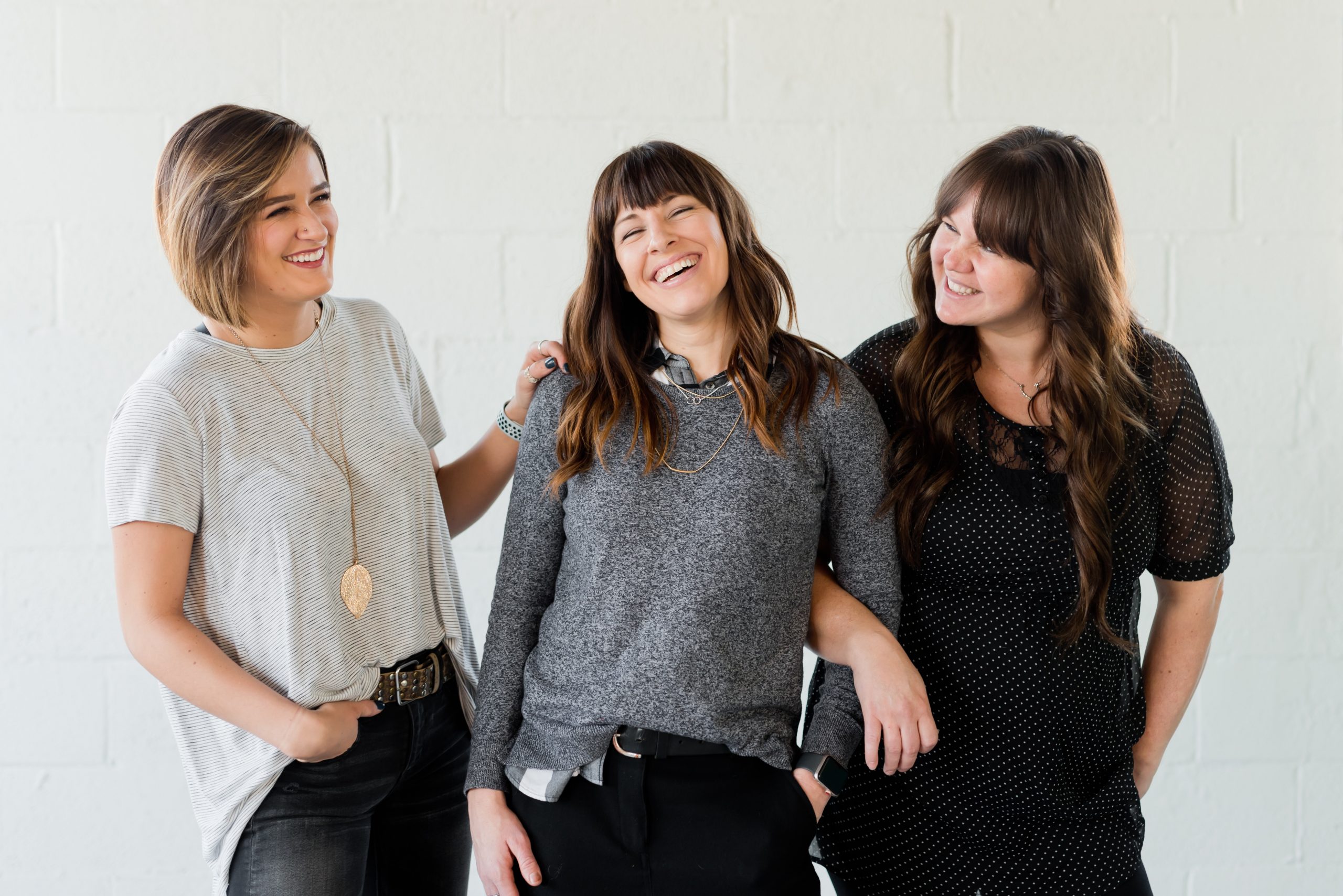 Photo by Aw Creative 3 women smiling and standing beside white wall